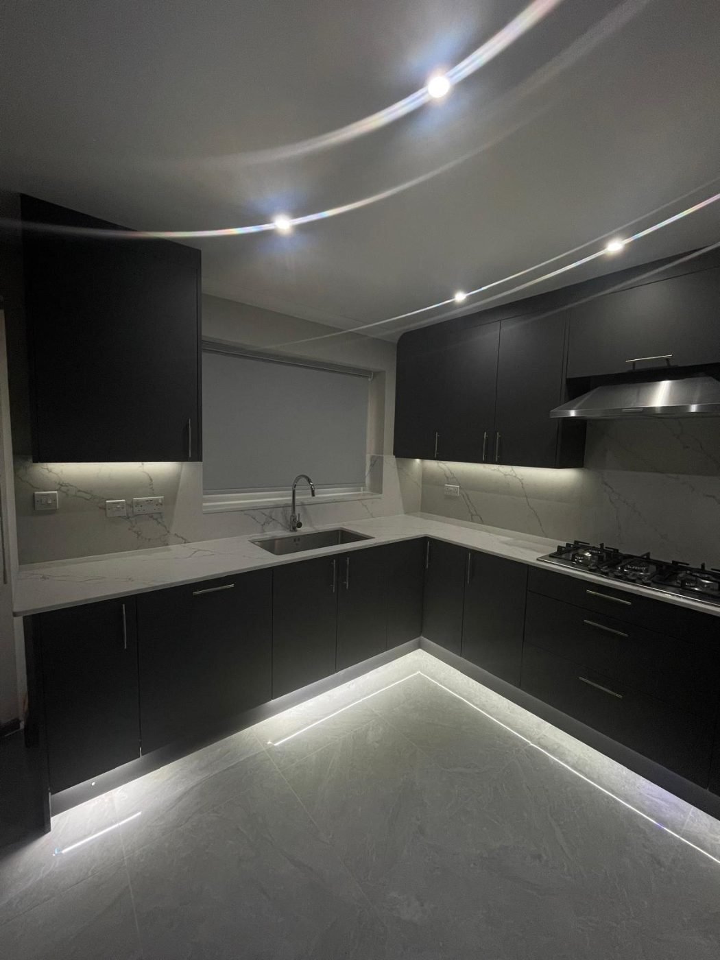 Dark handleless kitchen with marble worktops and LED plinth lighting by Kulwant Carpentry